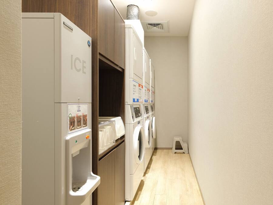 A laundry room with a front-loading washer and dryer, a small step stool, and a wooden cabinet.