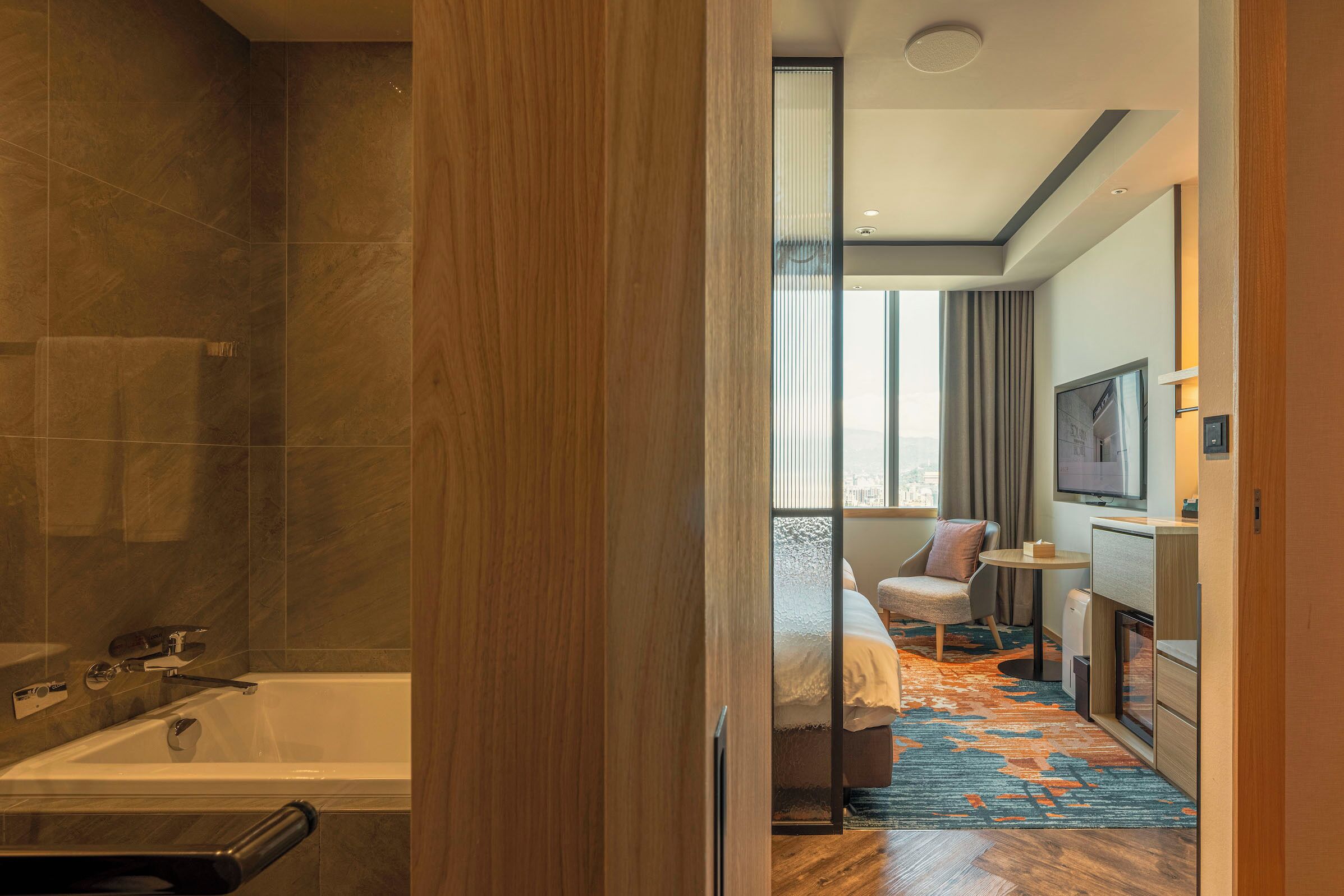 A modern bathroom with a bathtub and shower, a large window with curtains, and a view of the city.