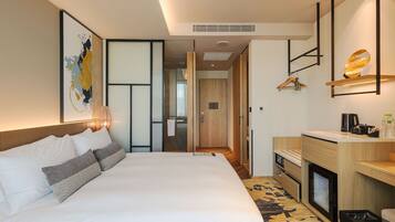 Quarto de hotel moderno com cama grande, escrivaninha de madeira, área de estar pequena e vista para o corredor.