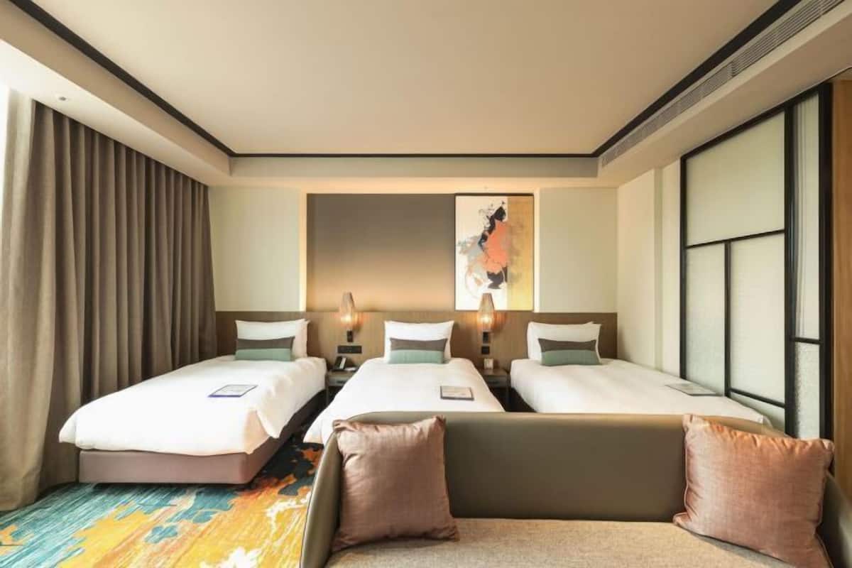 Een hotelkamer met twee bedden, een slaapbank, een groot raam en een schilderij aan de muur.