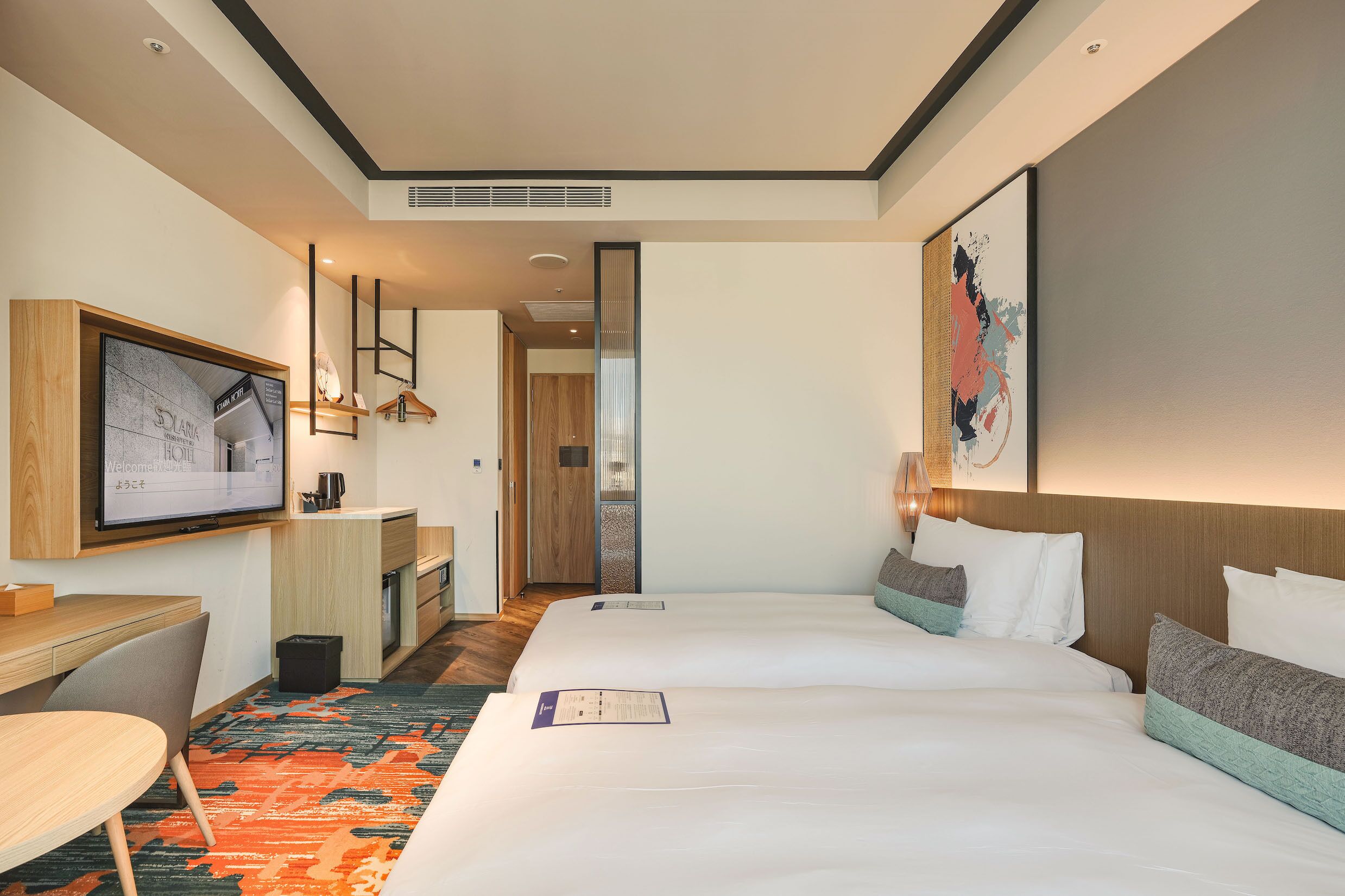 A hotel room with a bed, a desk, a TV, and a bathroom visible through an open door.