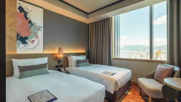 A hotel room with two beds, a desk, a chair, and a large window offering a city view.