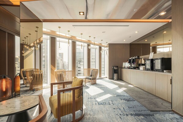 Un moderno hall de hotel con mobiliario de madera, ventanas amplias y una zona de cocina.