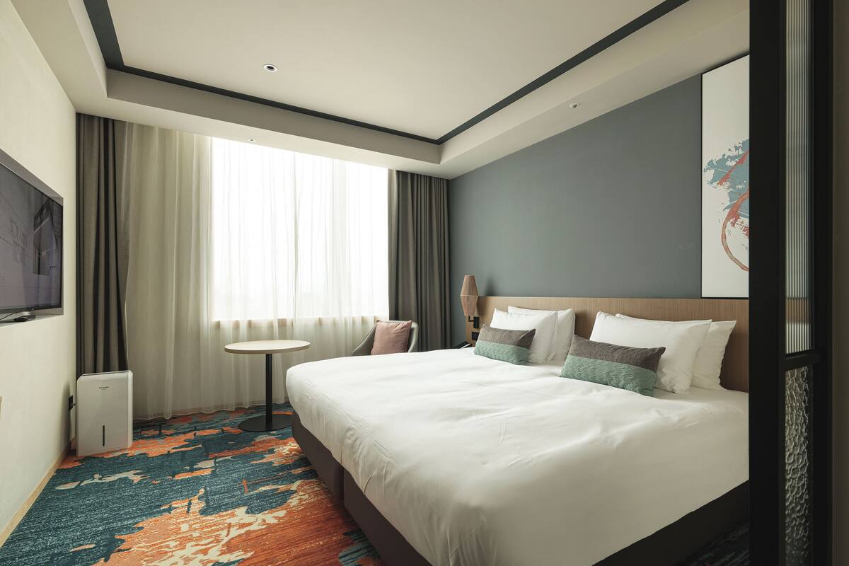 Een hotelkamer met een groot bed, een ronde tafel, een televisie en een raam met gordijnen.
