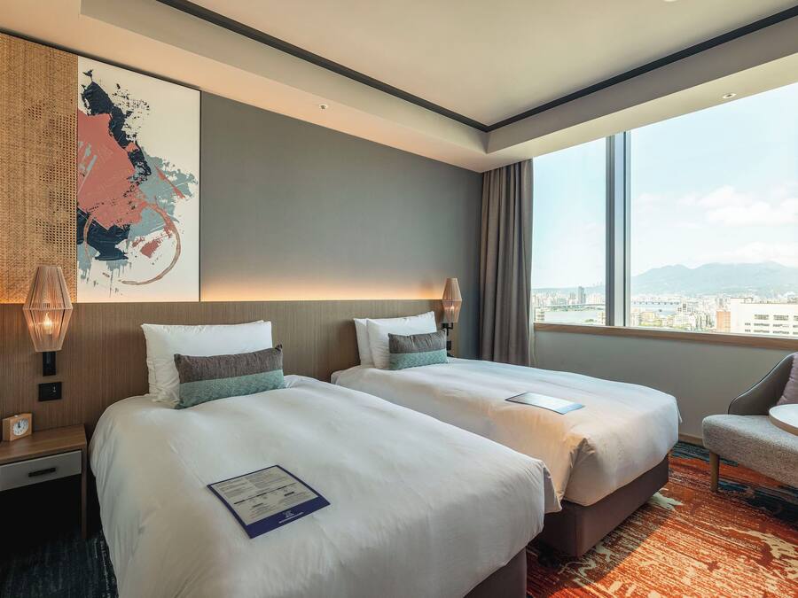 Ein Hotelzimmer mit zwei Betten, Blick auf die Stadt und einer kleinen Sitzecke.