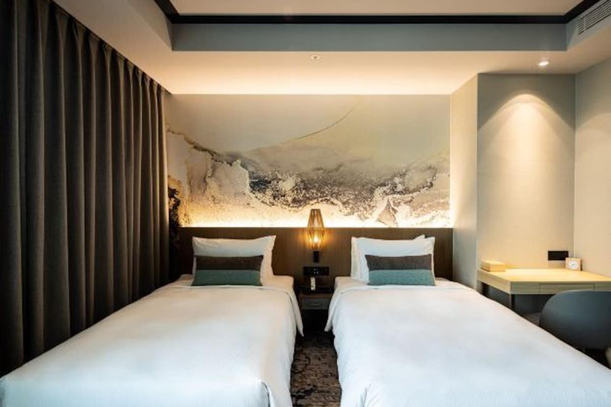 Een hotelkamer met twee bedden, een groot abstract kunstwerk aan de muur, een bureau en een stoel.