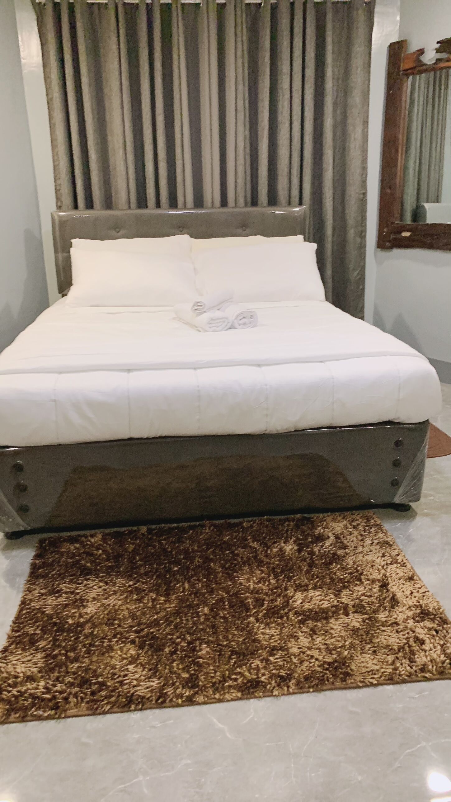 Una cama con ropa de cama blanca, un tapete marrón y un cabecero con listones verticales.