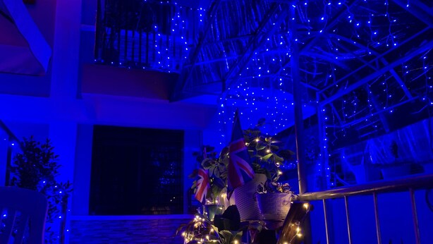 Ein Balkon mit blauer Beleuchtung, Blumentöpfen und einer Flagge.