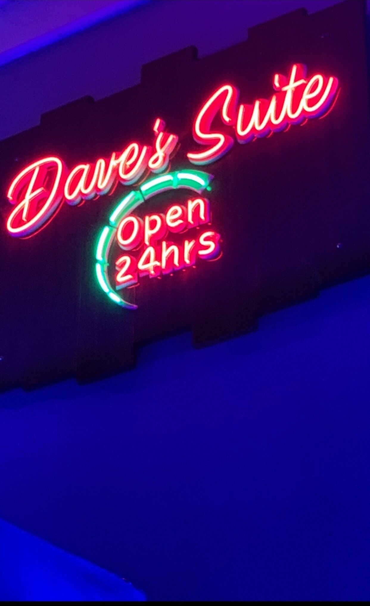Un letrero de neón con la inscripción "Dave's Suite" y "Abierto 24 horas", indicando que una suite de hotel está disponible las 24 horas.