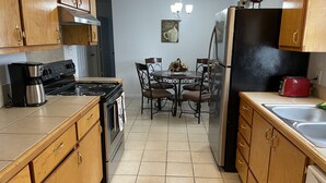 Une cuisine avec des meubles de rangement en bois, une cuisinière, un réfrigérateur, une table à manger avec des chaises et un lustre.