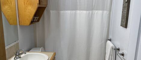 Une salle de bain avec un meuble-lavabo en bois, un lavabo blanc, des toilettes et un rideau de douche.