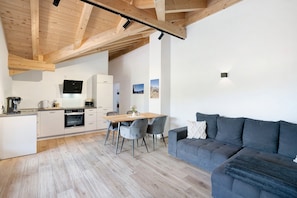 A modern kitchen with wooden beams, a dining area with chairs, and a gray sofa.