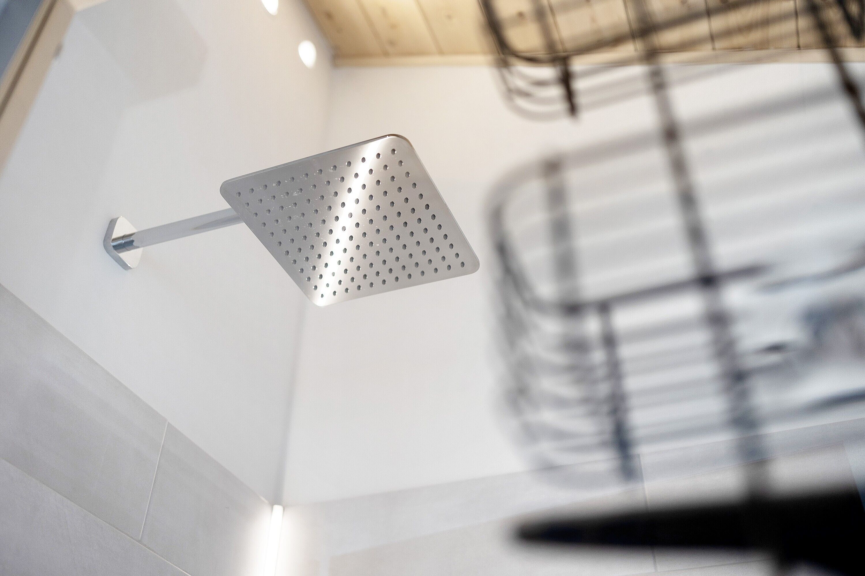 Ein moderner Duschkopf mit gelochtem Design, an einer Wand montiert, wobei die Deckenkonstruktion sichtbar ist.