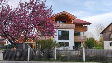 Ein zweistöckiges Gebäude mit einem Balkon, einem Holzzaun und einem Baum mit rosa Blüten.