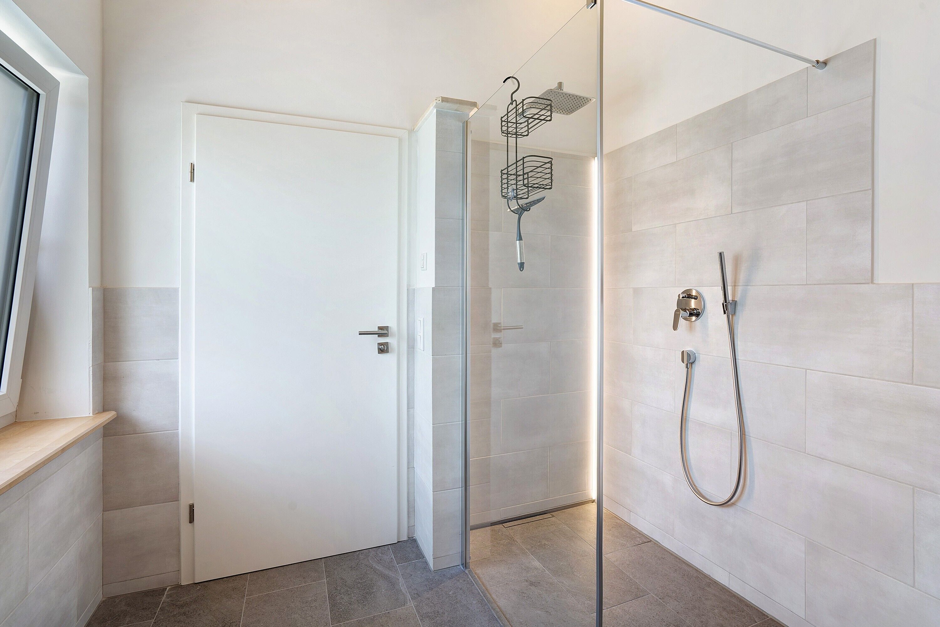 A modern bathroom with a glass shower enclosure, a white door, and a showerhead.