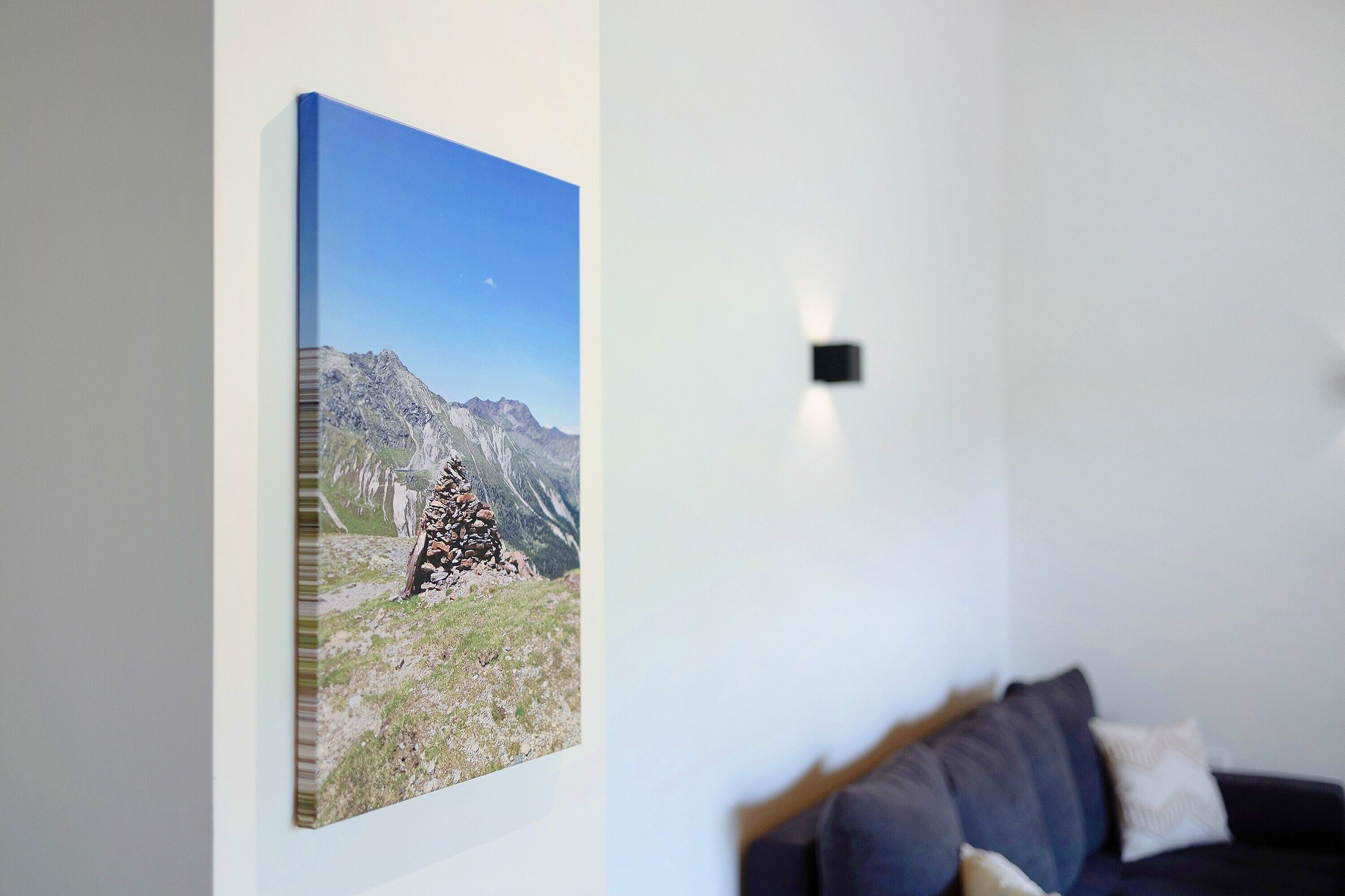 Una habitación con un cuadro de un paisaje montañoso en la pared, un sofá de color oscuro y una pequeña lámpara negra.
