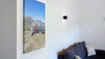 Una habitación con un cuadro de un paisaje montañoso en la pared, un sofá de color oscuro y una pequeña lámpara negra.