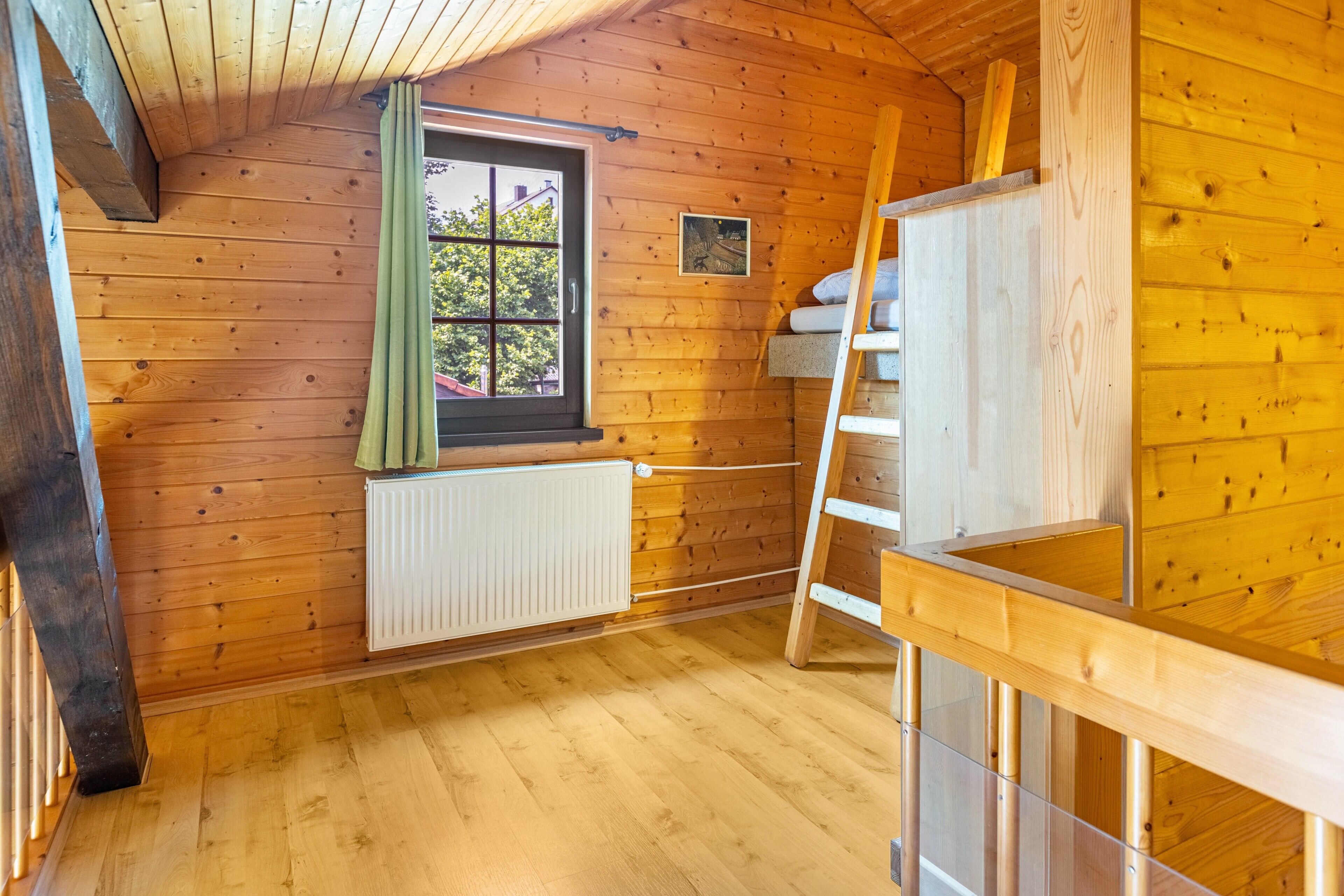 A wooden interior with a window, radiator, and wooden ladder.