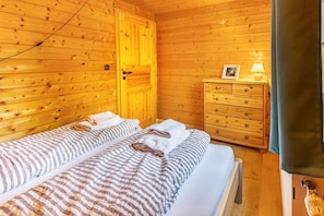 Une chambre dans un chalet en bois, avec deux lits, une commode en bois et une lampe.
