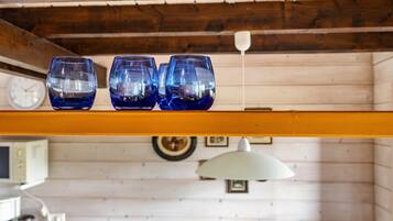 Three blue glasses on a wooden shelf in a room with wooden walls, a clock, and a hanging lamp.