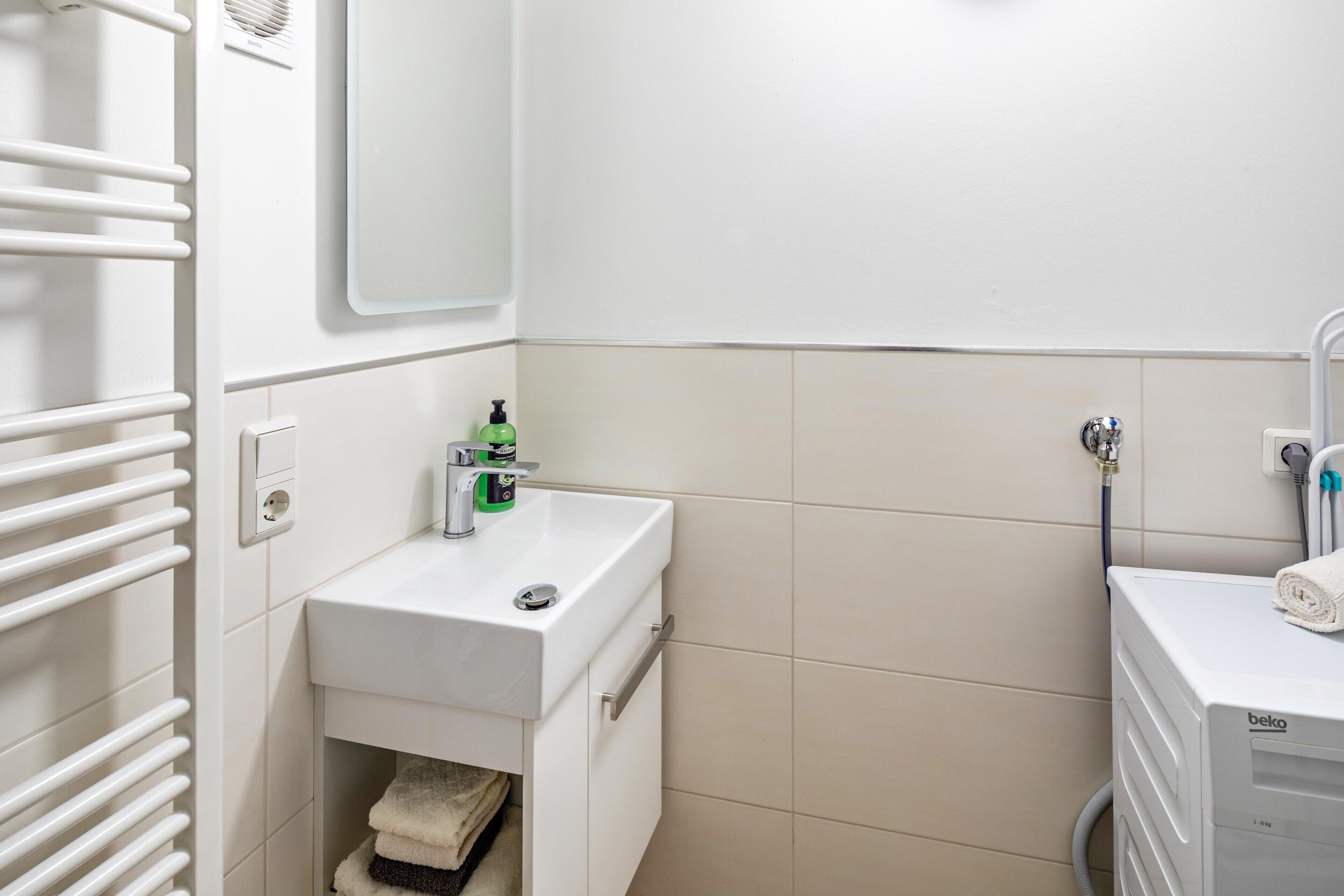 A bathroom with a white sink, a mirror, a towel rack, and a towel dispenser.