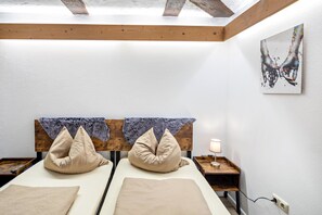 A room with two beds, a wooden headboard, a small bedside table with a lamp, and a painting on the wall.