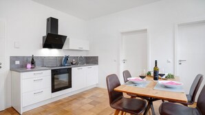 A modern kitchen with white cabinetry, a built-in oven, and a dining area with a wooden table and leather chairs. - Apartment "Goldberg" - Living in the Winery (Grünstadt)
