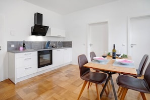 A modern kitchen with white cabinetry, a built-in oven, and a dining area with a wooden table and leather chairs. - Apartment "Goldberg" - Living in the Winery (Grünstadt)