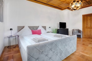 A bedroom with a large bed, a television, a chair, and a wooden ceiling.