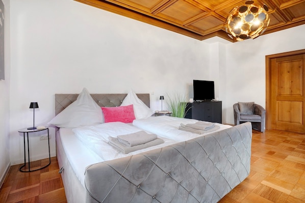 Une chambre à coucher avec un lit, des tables de chevet, une télévision, une chaise et un plafond en bois.