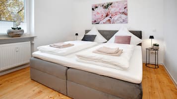 Un letto matrimoniale con testiera grigia rivestita in tessuto, biancheria da letto bianca e un grande quadro con fiori sopra.