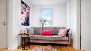 A modern living room with a grey sofa, a pink cushion, a small side table with vases, and a fluffy rug.