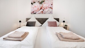 A hotel room with two beds, a headboard, bedside tables, lamps, and a floral artwork on the wall.