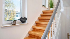 A staircase with wooden steps, a white railing, and a window with a view of trees and a house.
