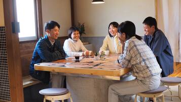 Un grupo de personas sentadas alrededor de una mesa de madera con base de concreto, en una habitación con paredes de madera y una lámpara colgante.