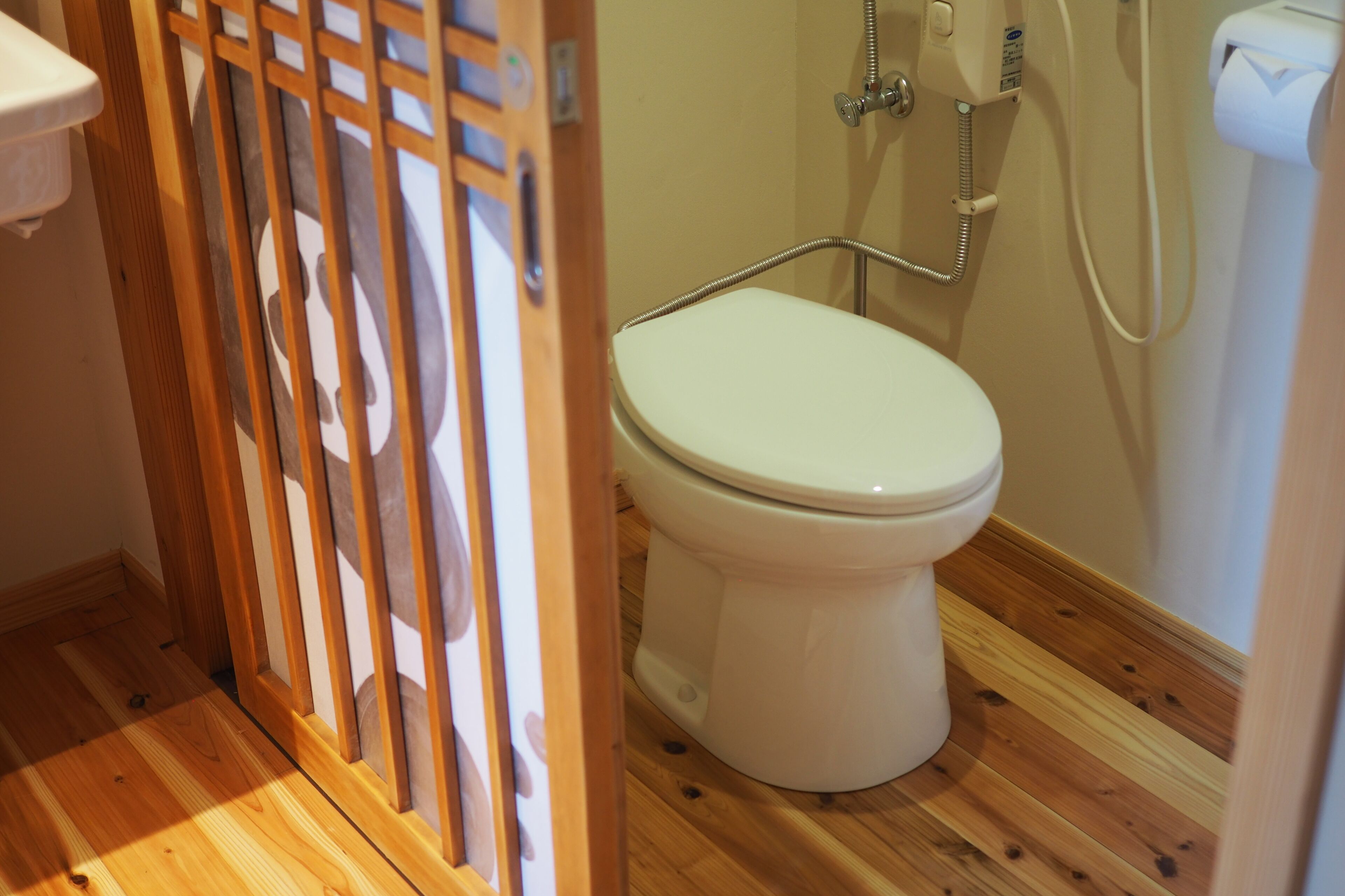 Un baño con inodoro, suelo de madera y ducha con manguera.