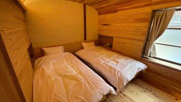 A small, cozy room with two beds, wooden walls, and a window with curtains.