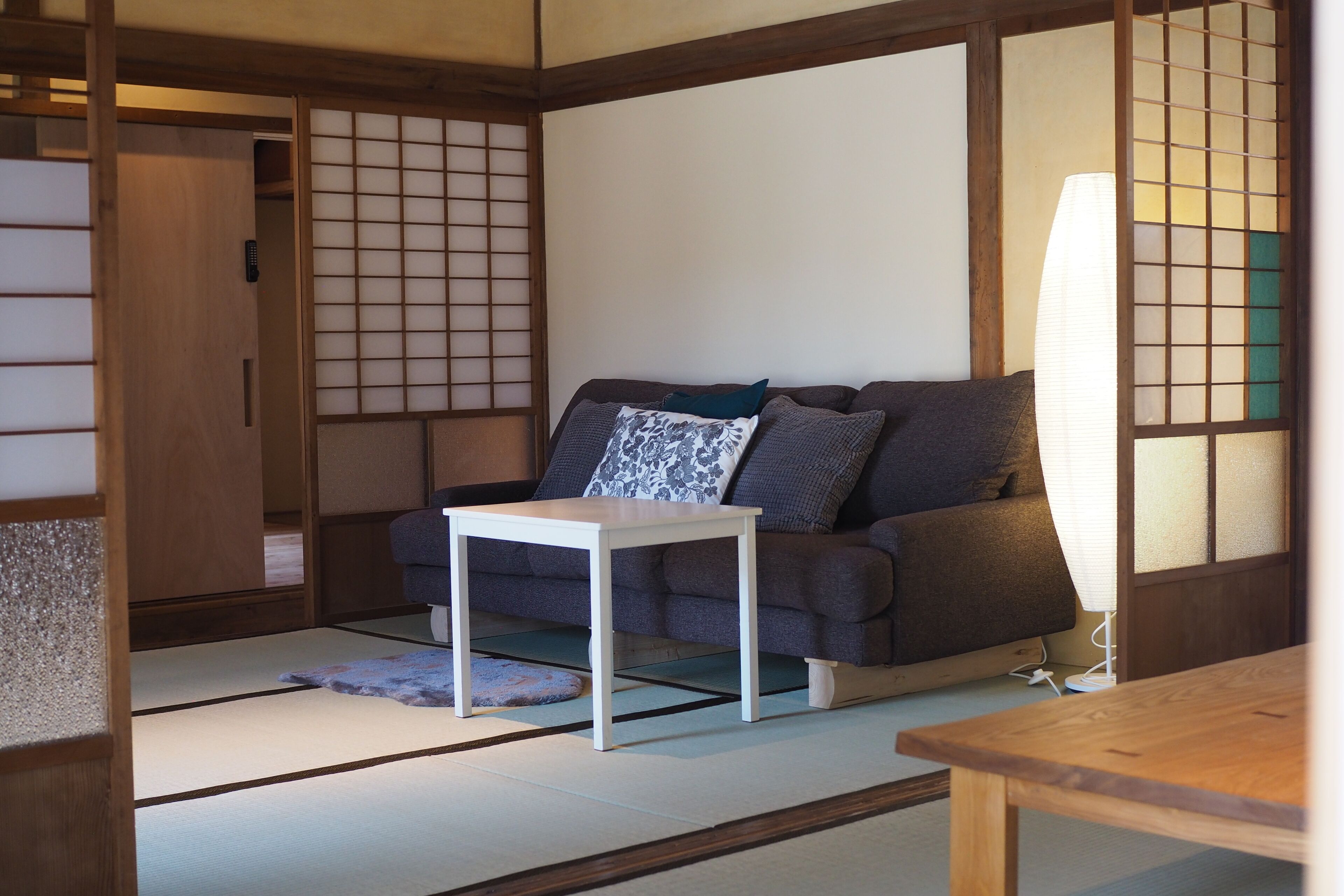 Et traditionelt japansk rum med tatamimåtter, et lavt træbord, en sofa med puder og skydedøre i shoji-stil.