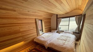 A cozy bedroom with wooden walls, a large bed, a window with curtains, and a colorful rug. - okatei (Tonosho)