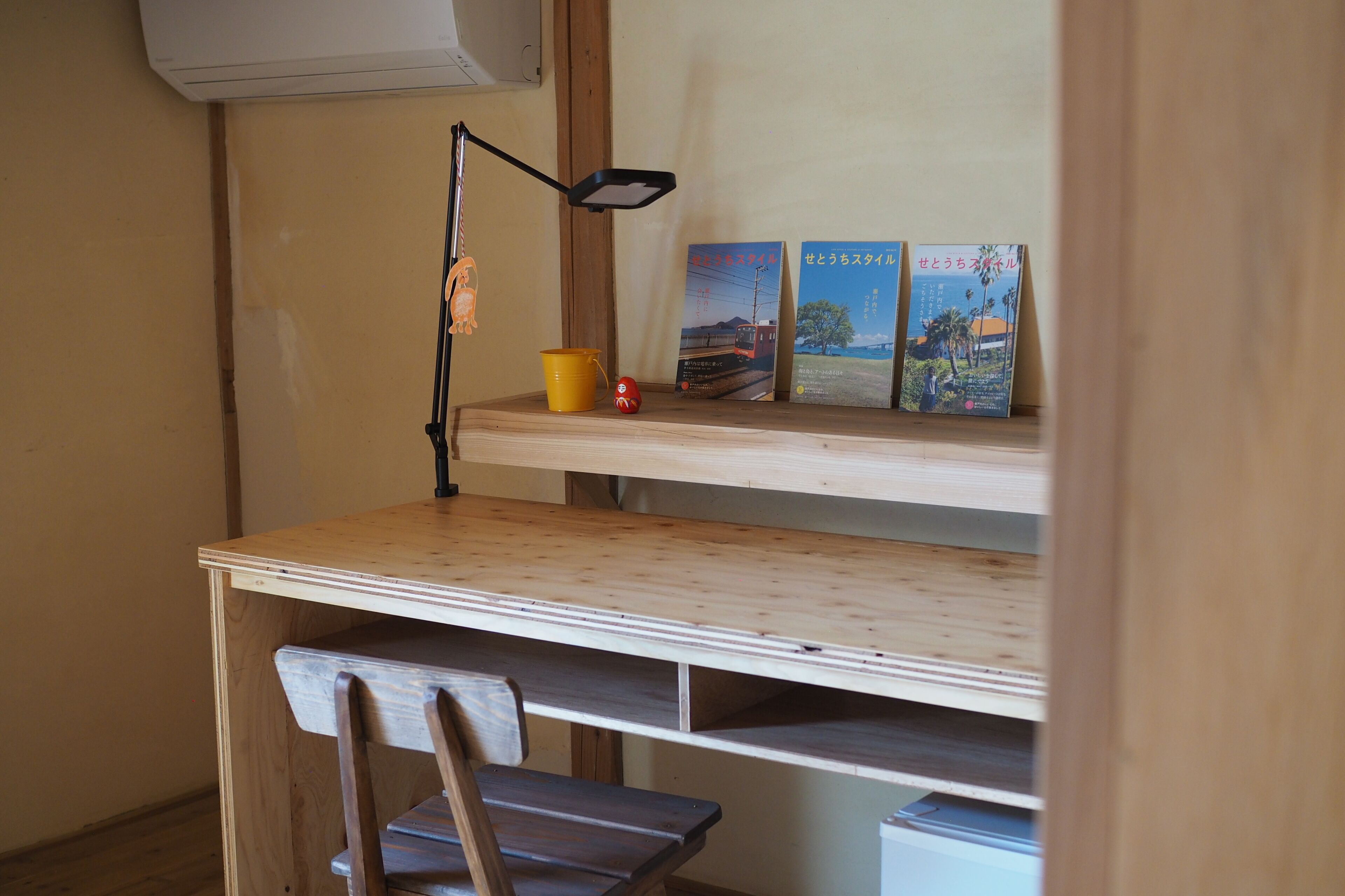 Een compacte werkplek met een bureau, stoel en een plank met boeken en een lamp.