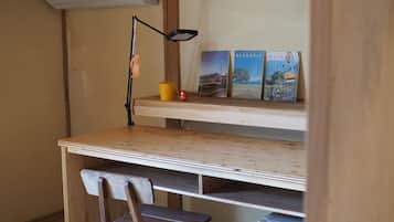 Ein kleiner Arbeitsbereich mit Schreibtisch, Stuhl und einer Regal mit Büchern und einer Lampe.