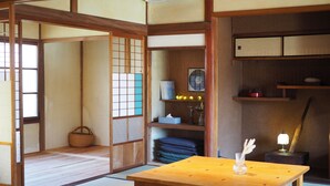 A traditional Japanese room with tatami flooring, a wooden table, a fan, and a shelf with various items. - okatei (Tonosho)