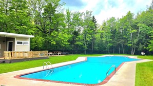 Ein rechteckiger Pool mit Holzdeck und Metallleiter, umgeben von Rasen und Bäumen.