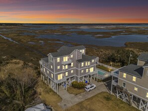 Una casa a più piani con un balcone, una piscina e vista su una zona umida al tramonto.