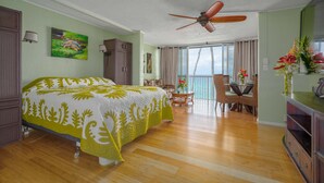 A hotel room with a bed, a dining area, a balcony, and a ceiling fan. - spectacular ocean front studio condo,  Magic sands, ideal view and location (Kailua-Kona)