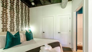 Habitación de hotel con una cama grande, dos puertas, una pared con un diseño decorativo y un baño visible.