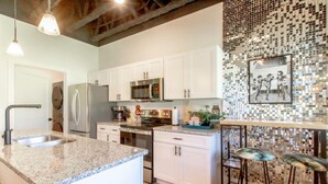Una cocina moderna con armarios blancos, encimera de granito, electrodomésticos de acero inoxidable y salpicadero de mosaicos.