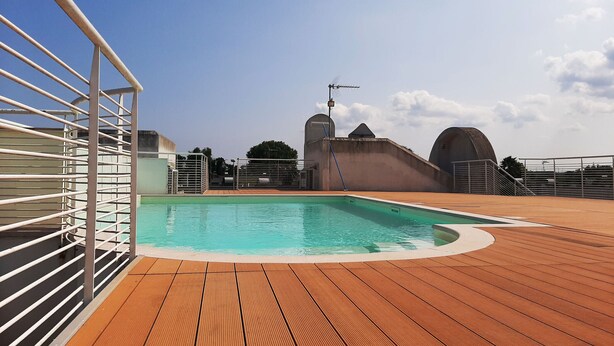 Ein Schwimmbecken mit Holzterrasse, Metallgeländern und blauem Himmel.