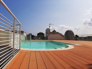 En swimmingpool med træterrasse, metalgelændere og en klar himmel.