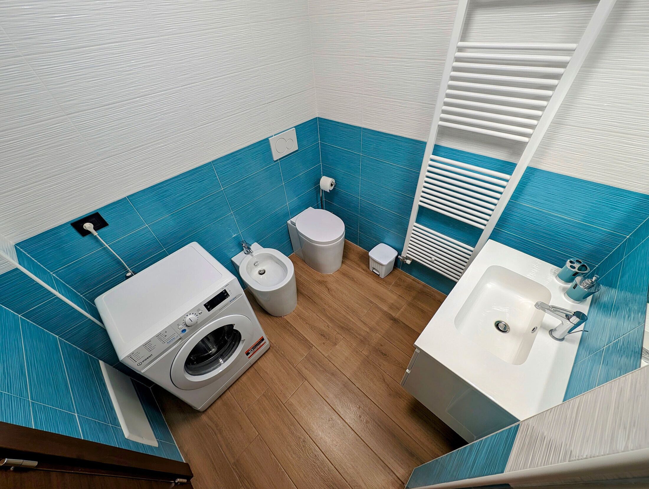 A compact bathroom with a washing machine, toilet, bidet, and sink.